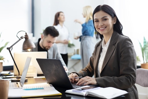 femme souriante au travail devant son ordinateur avec des collegues derriere elle